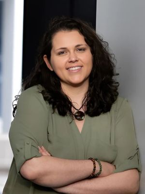 Tai Ma, founder of Shaman Tai Ma LLC, smiling with arms crossed, contributing her expertise in mindfulness, somatic healing, and trauma-informed practices as a project collaborator at JVR Strategies.